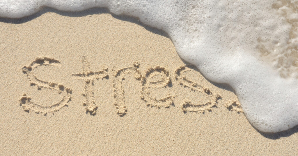 Waves washing away the word "stress" in the sand.